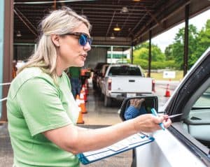 YEC staffer, Amy Crocker, standing at the drive-thru lane with clipboard in hand as she returns an identification card to a member through his driver-side window.