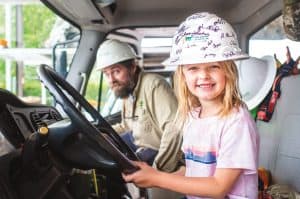A smiling Jordyn Hart at the wheel of a YEC utility truck with lineman John Elliott in the passenger seat.