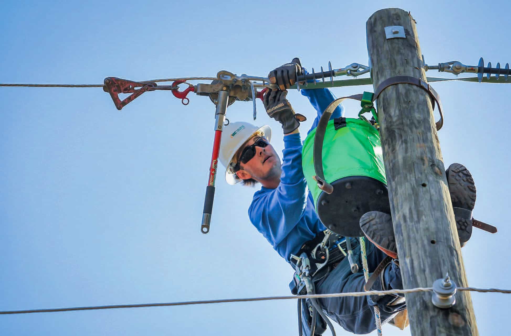 Lineworker, Jackson Good, outfitted in safety gear at the top of an electric utility pole