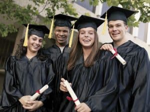 Four smiling graduates outside holding diplomas